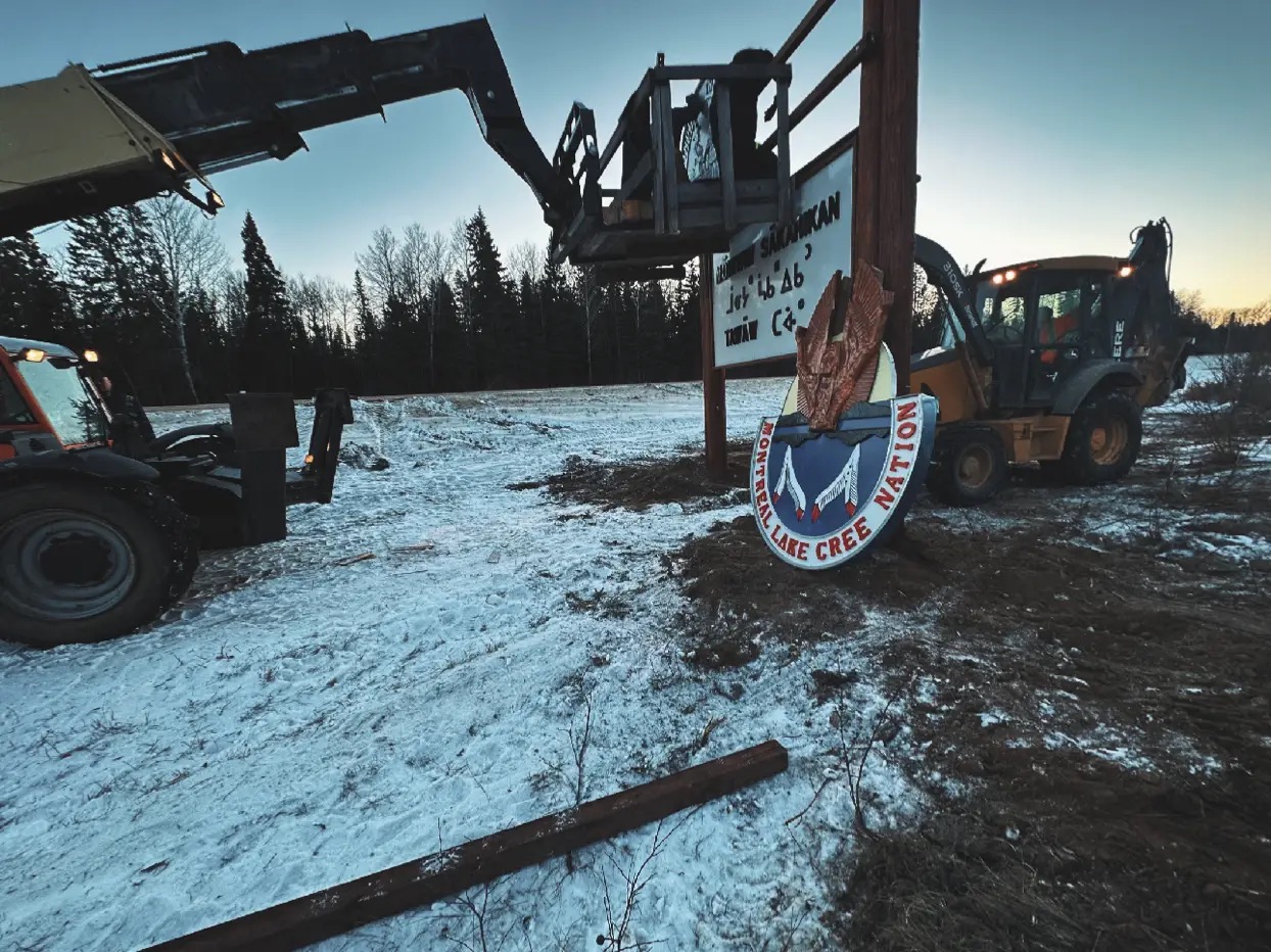 Montreal Lake Cree Nation crest being installed with telehandler and backhoe during Moniyaw Sakahikan sign erection