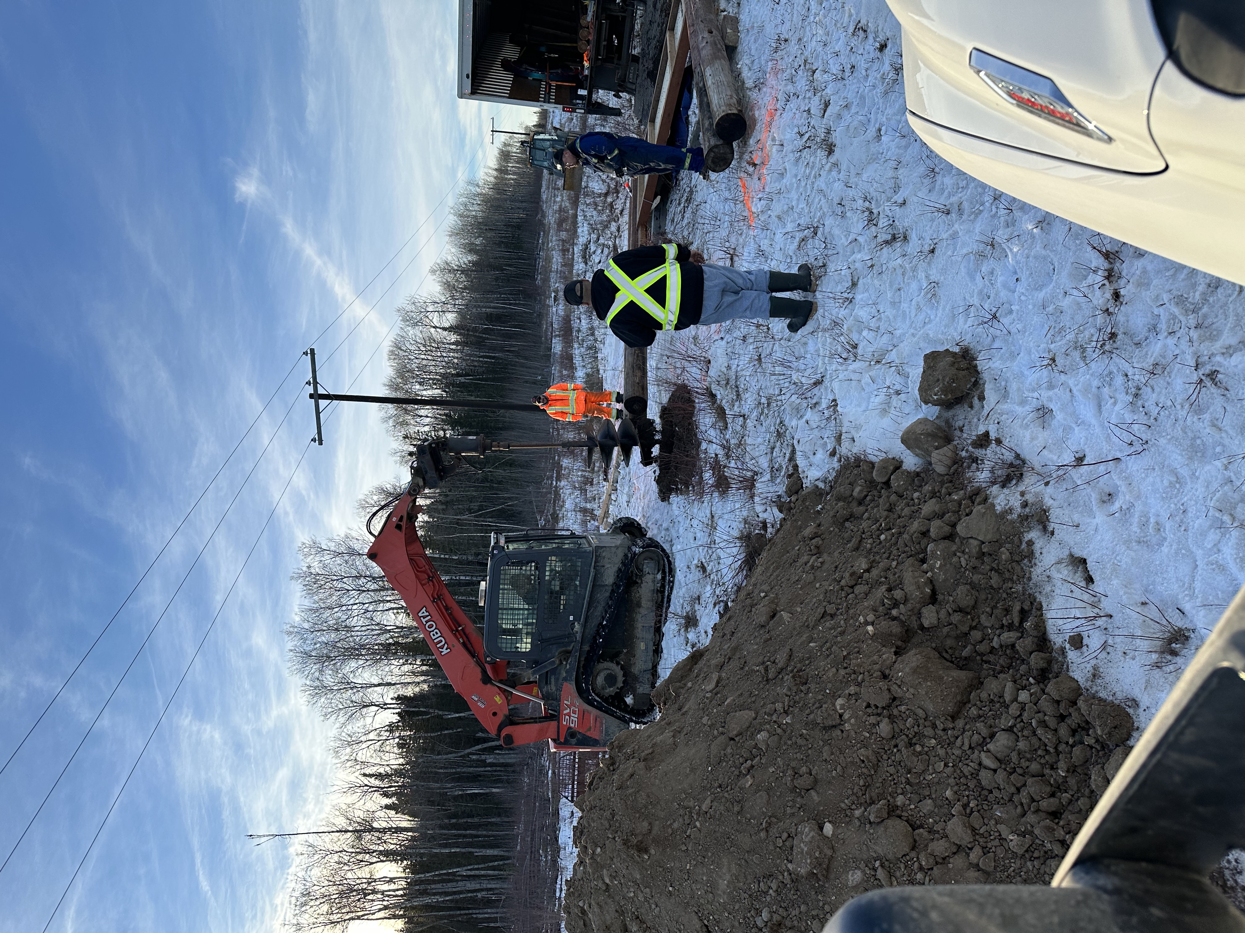 Skid-steer and crew excavating sign post footings in winter at Moniyaw Sakahikan site
