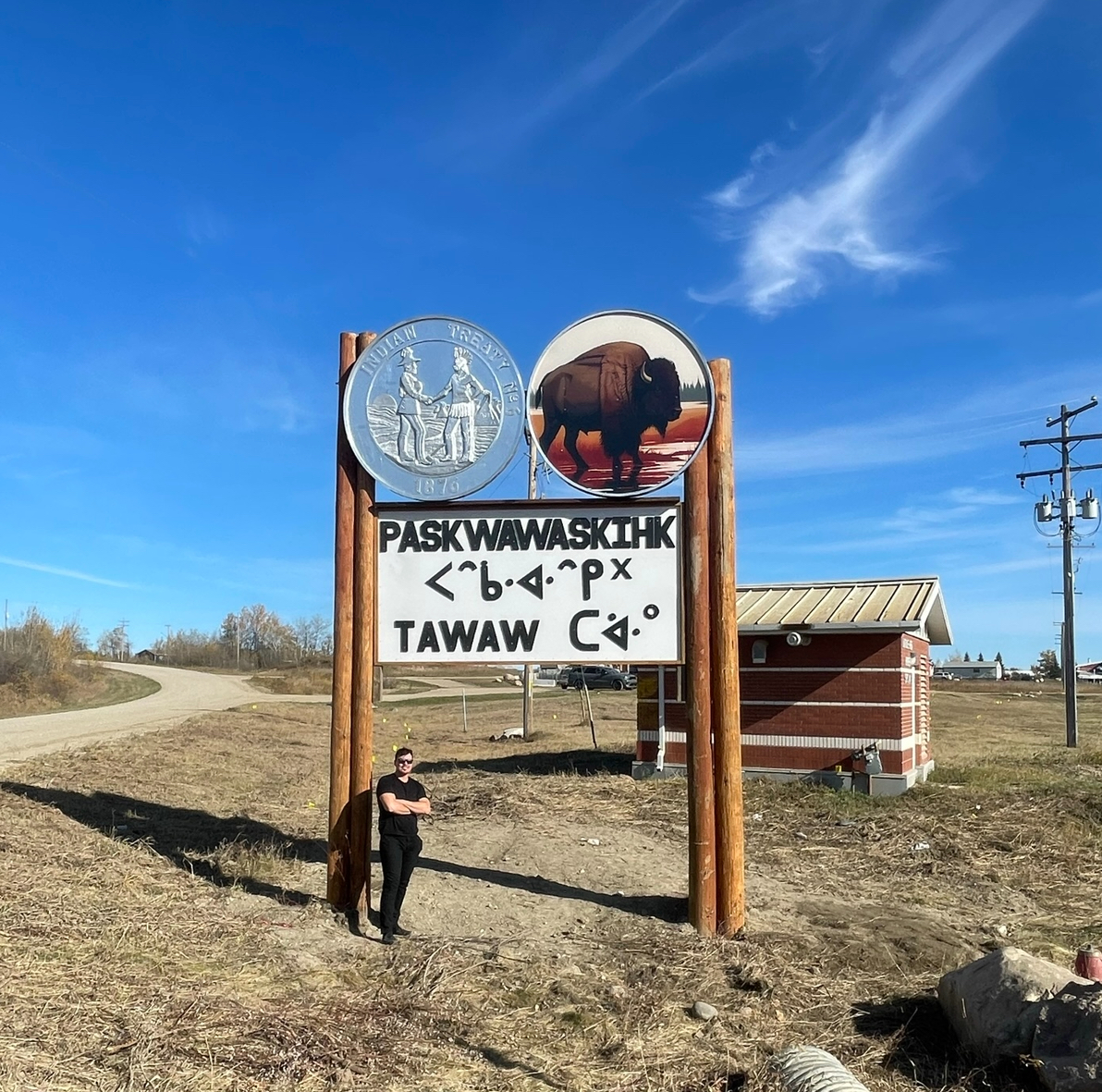Paskwawaskihk Treaty 6 entrance sign with bison medallion in daylight, Iron Alliance Construction crew on site