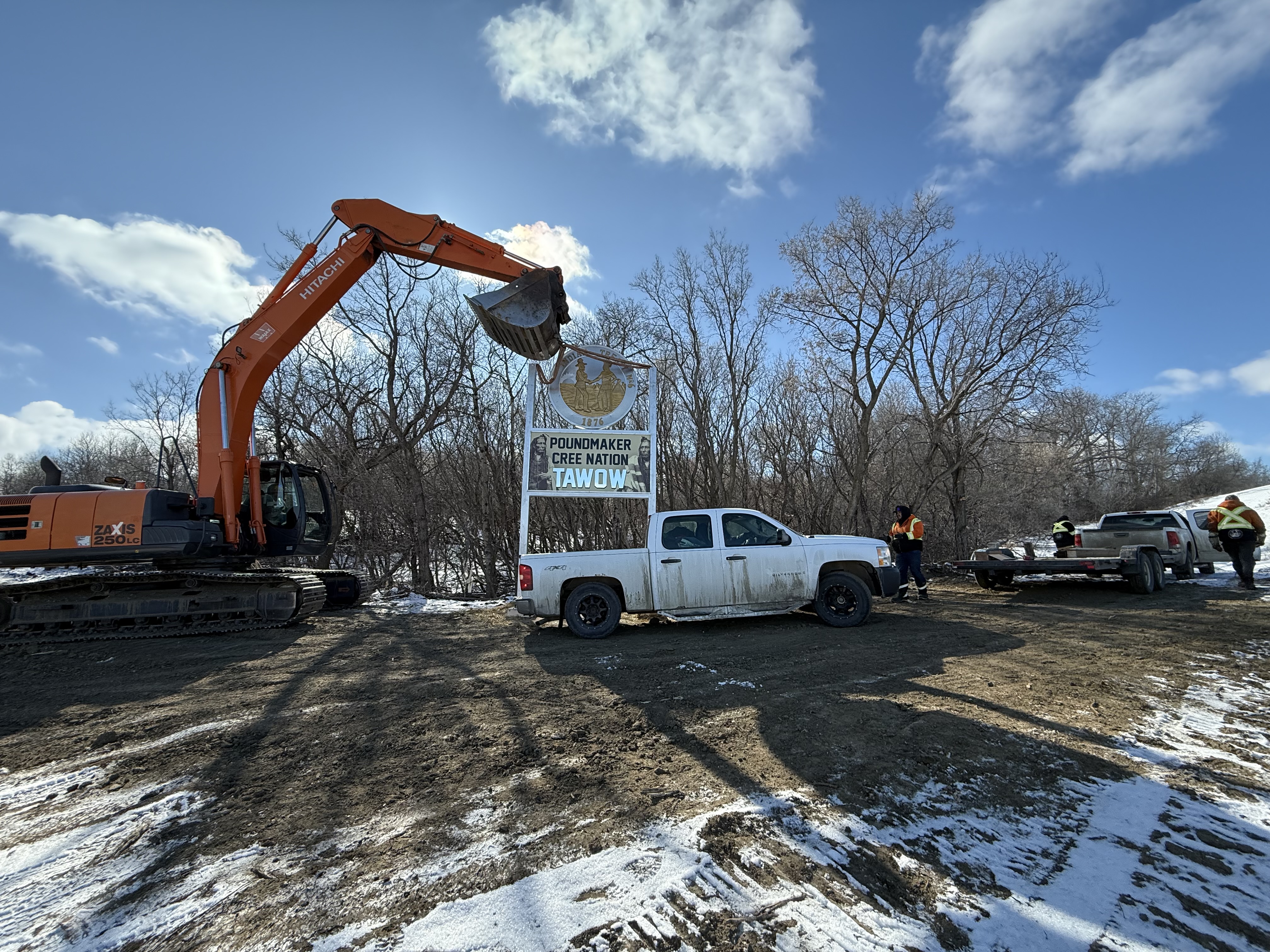 Poundmaker Cree Nation sign during installation with excavator and crew on site