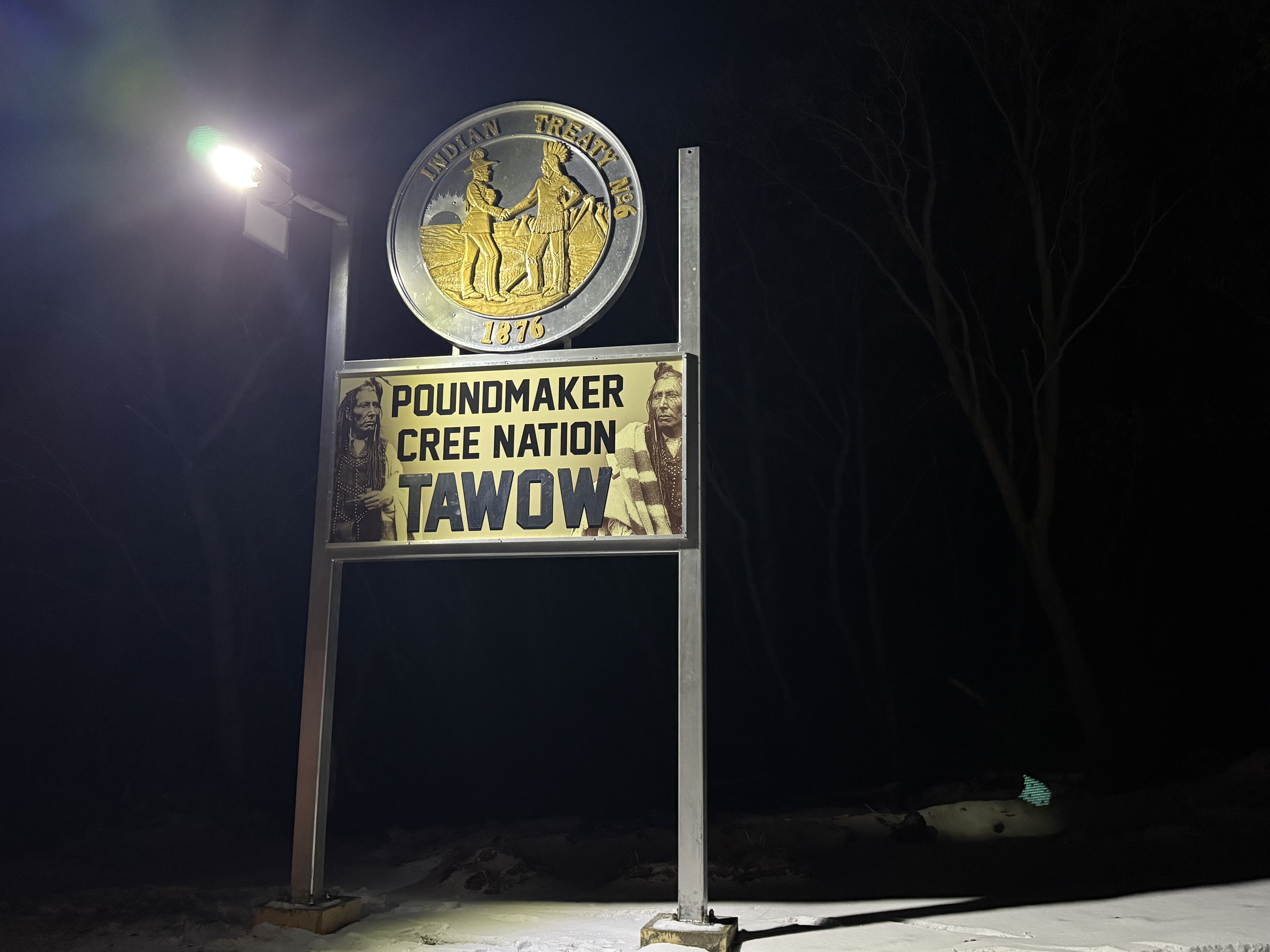 Poundmaker Cree Nation Tawow entrance sign with Treaty 6 medallion, illuminated at night
